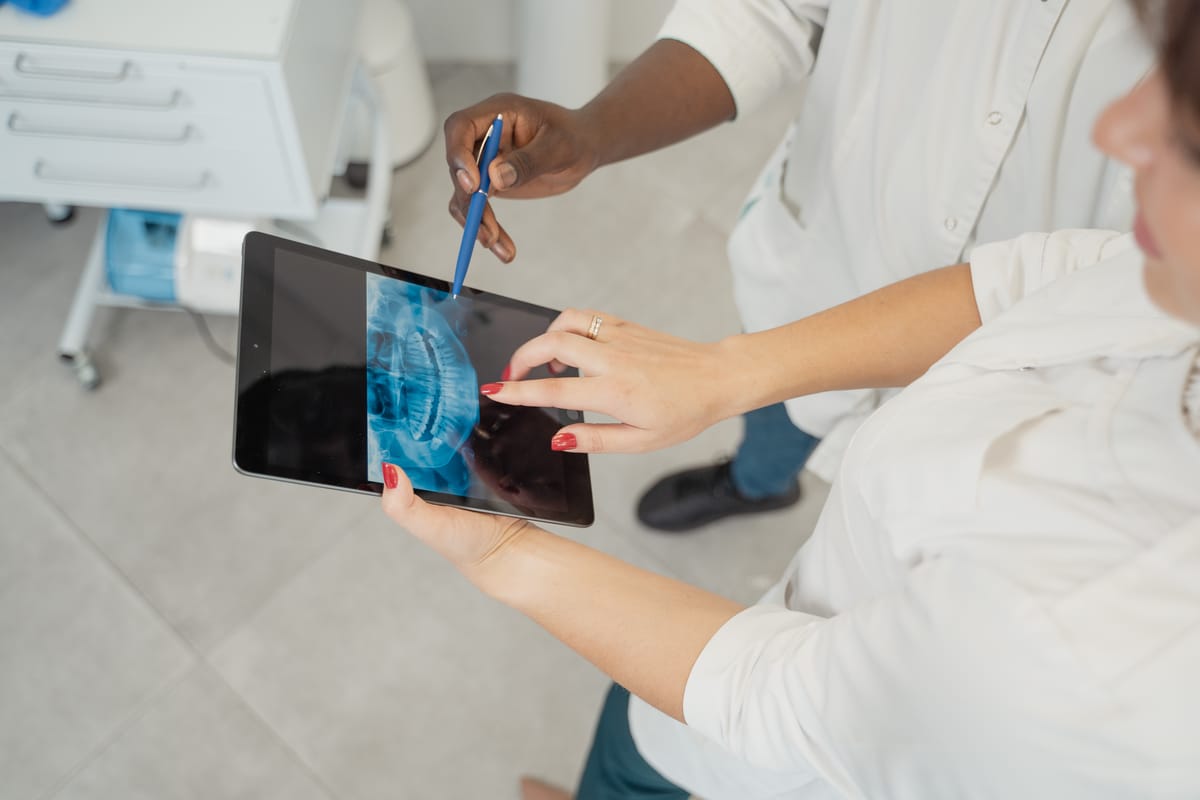 Indian dentist dictating a visit note chairside with a patient and tablet